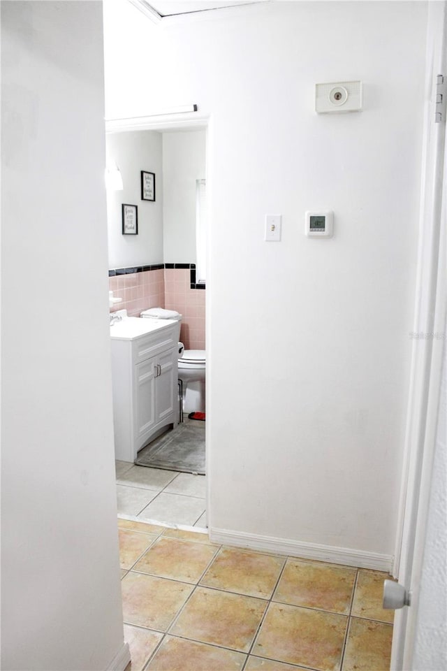 bathroom with toilet, vanity, tile patterned floors, and tile walls