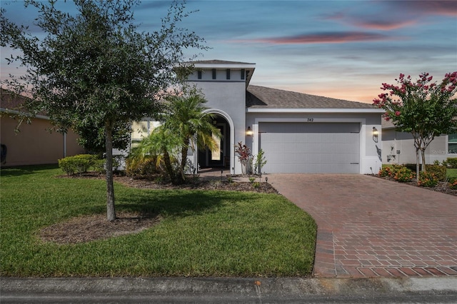 view of front facade with a garage, a shingled roof, decorative driveway, stucco siding, and a front yard