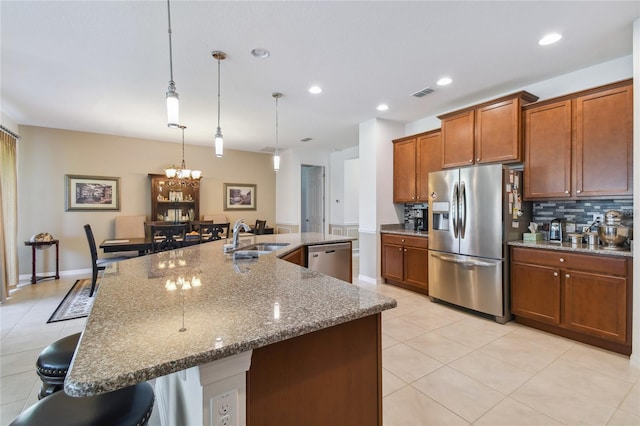 kitchen with appliances with stainless steel finishes, tasteful backsplash, sink, light tile patterned floors, and a large island with sink