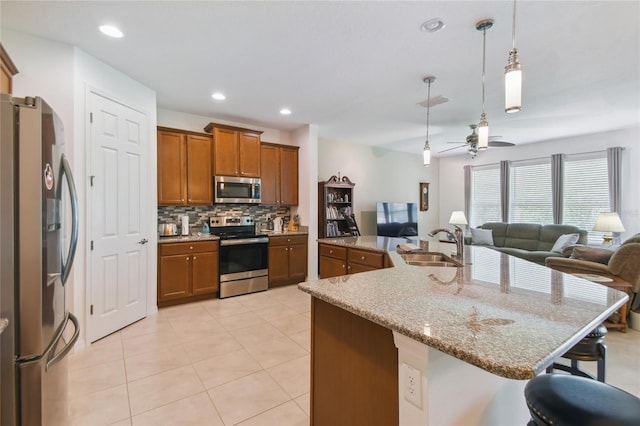 kitchen with a kitchen bar, appliances with stainless steel finishes, light stone counters, backsplash, and ceiling fan