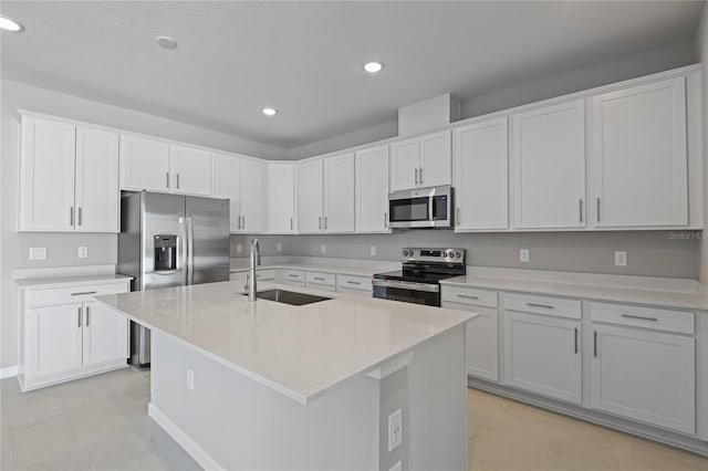 kitchen featuring sink, light stone counters, an island with sink, stainless steel appliances, and white cabinets