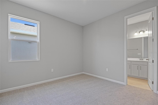 unfurnished bedroom with ensuite bathroom, sink, and light carpet