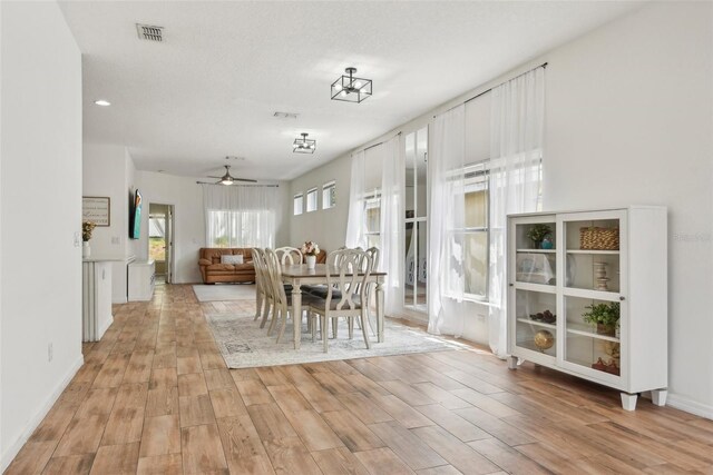 unfurnished dining area with a textured ceiling, light wood-type flooring, and ceiling fan