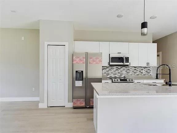 kitchen featuring stainless steel appliances, sink, light hardwood / wood-style floors, decorative light fixtures, and white cabinetry