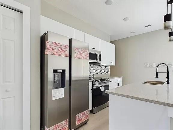 kitchen featuring white cabinetry, tasteful backsplash, sink, light hardwood / wood-style floors, and appliances with stainless steel finishes