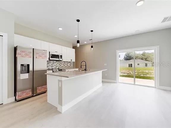 kitchen featuring tasteful backsplash, stainless steel appliances, a center island with sink, white cabinets, and decorative light fixtures