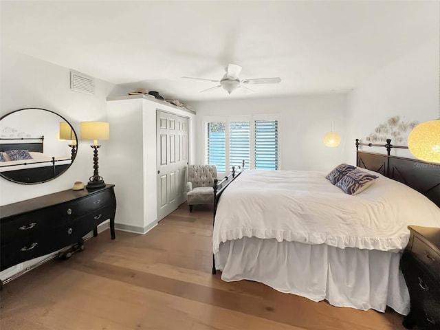 bedroom featuring wood finished floors, visible vents, baseboards, a ceiling fan, and a closet