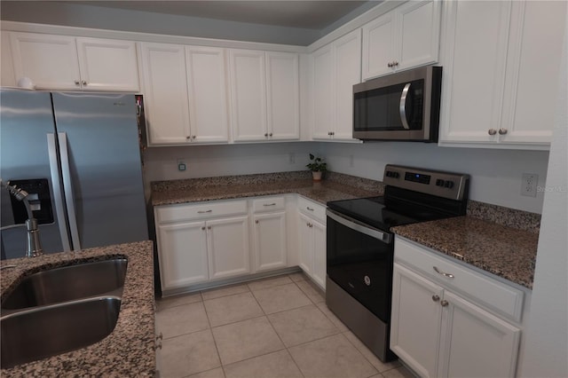 kitchen featuring light tile patterned floors, appliances with stainless steel finishes, dark stone countertops, and white cabinetry