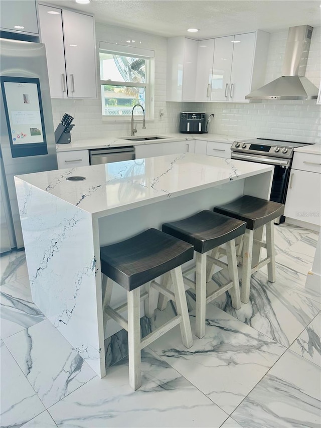 kitchen with wall chimney range hood, sink, a kitchen breakfast bar, a center island, and white cabinets