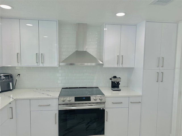 kitchen with wall chimney exhaust hood, tasteful backsplash, stainless steel electric stove, light stone countertops, and white cabinets