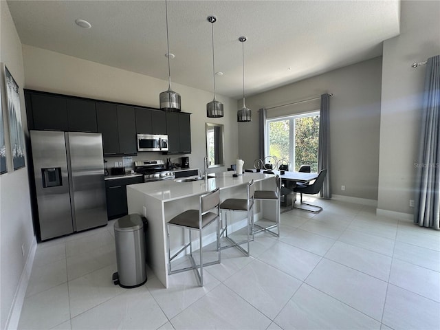 kitchen with a kitchen island with sink, decorative light fixtures, appliances with stainless steel finishes, and light tile patterned floors