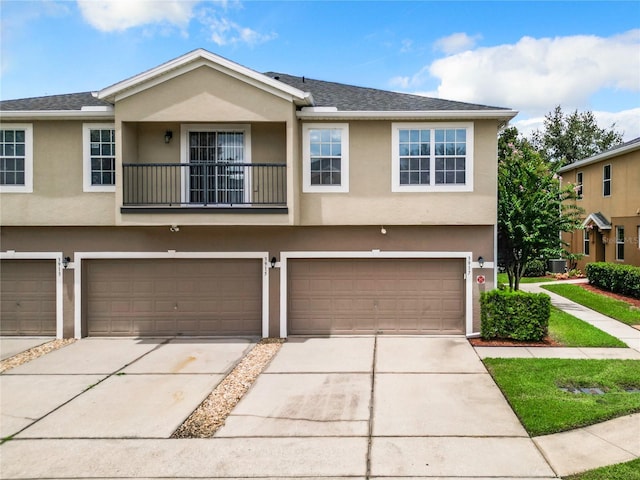 townhome / multi-family property with driveway, a balcony, a garage, and stucco siding