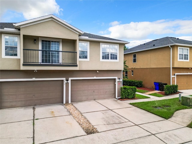 multi unit property featuring driveway, an attached garage, a balcony, and stucco siding