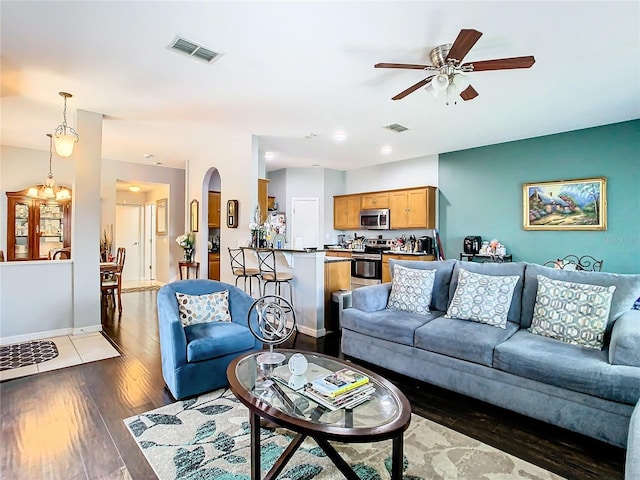 living area featuring dark wood-type flooring, arched walkways, visible vents, and ceiling fan with notable chandelier