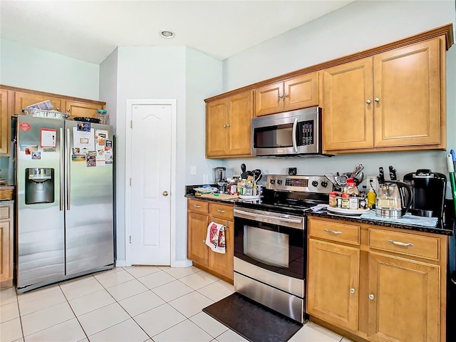 kitchen with light tile patterned floors, appliances with stainless steel finishes, brown cabinetry, and dark stone countertops