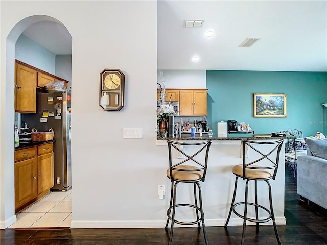 kitchen with visible vents, arched walkways, dark countertops, brown cabinets, and a kitchen breakfast bar