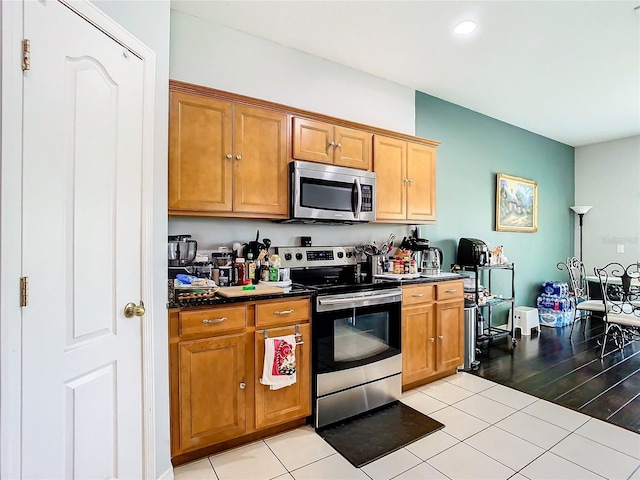 kitchen featuring brown cabinets, light tile patterned floors, dark countertops, recessed lighting, and appliances with stainless steel finishes