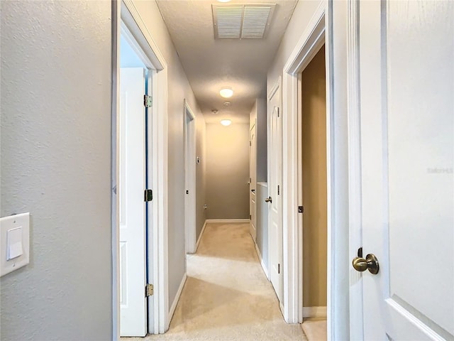 corridor featuring light colored carpet, visible vents, a textured wall, and baseboards