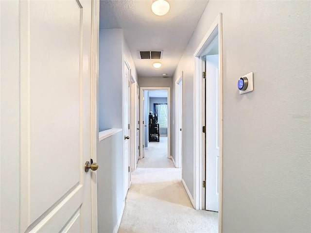 hallway featuring visible vents, light carpet, and baseboards