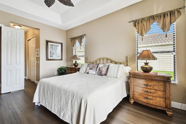 bedroom with a raised ceiling, a closet, dark hardwood / wood-style floors, and ceiling fan