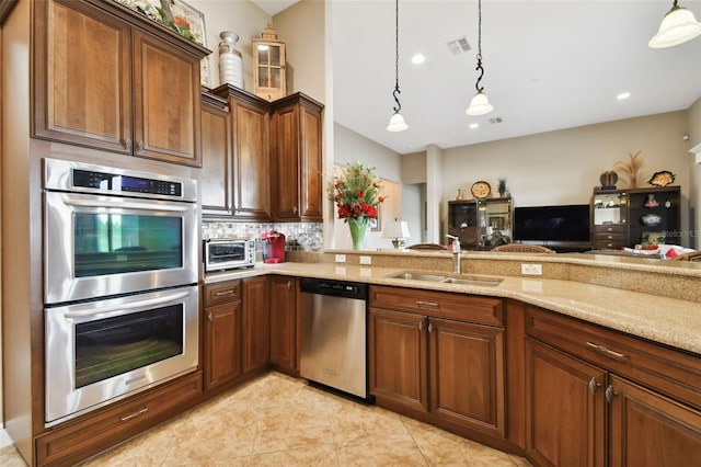 kitchen featuring sink, appliances with stainless steel finishes, hanging light fixtures, light stone counters, and decorative backsplash