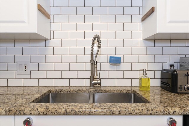 kitchen featuring decorative backsplash, sink, stone countertops, and white cabinetry