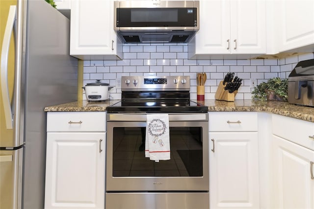 kitchen with tasteful backsplash, stainless steel appliances, dark stone countertops, and white cabinetry