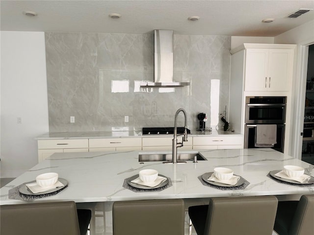 kitchen with decorative backsplash, a breakfast bar area, light stone countertops, and wall chimney range hood