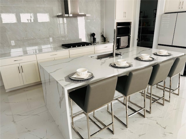 kitchen with double wall oven, light stone countertops, wall chimney range hood, and a large island