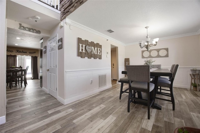 dining space featuring a notable chandelier, crown molding, wood-type flooring, and a textured ceiling