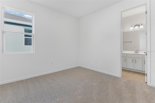 unfurnished bedroom featuring sink, ensuite bath, and light colored carpet