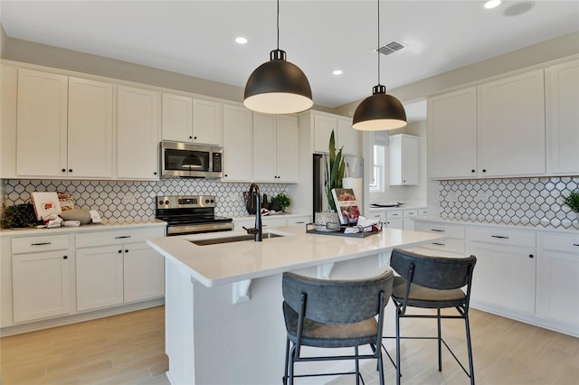 kitchen with sink, white cabinetry, decorative light fixtures, appliances with stainless steel finishes, and a kitchen island with sink