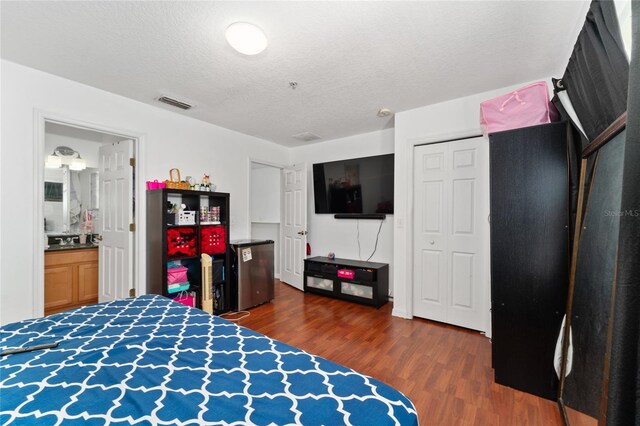 bedroom featuring dark wood-type flooring, fridge, ensuite bathroom, and a textured ceiling