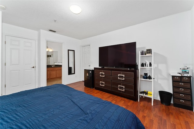 bedroom featuring ensuite bath and dark wood-type flooring