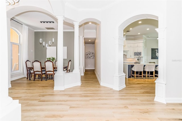 hall with decorative columns, sink, light wood-type flooring, and ornamental molding