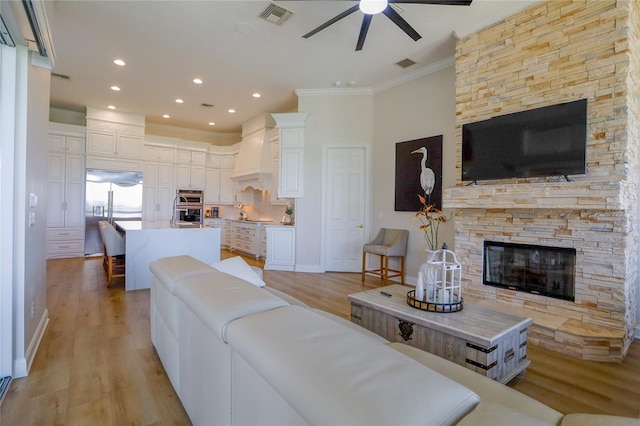 living room featuring a fireplace, ornamental molding, light hardwood / wood-style floors, and ceiling fan