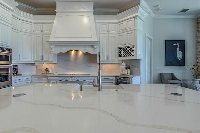 kitchen with light stone counters, premium range hood, crown molding, and white cabinets