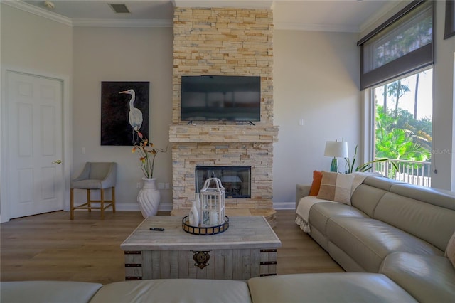 living room featuring crown molding, a stone fireplace, and light wood-type flooring