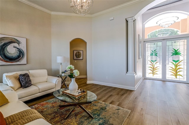 living room featuring crown molding, an inviting chandelier, decorative columns, light hardwood / wood-style floors, and french doors