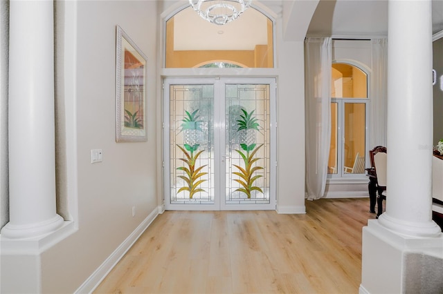 foyer entrance featuring decorative columns, wood-type flooring, an inviting chandelier, and french doors