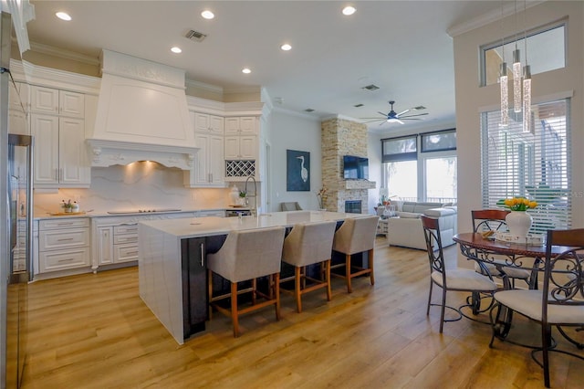 kitchen with custom exhaust hood, white cabinets, and a center island with sink