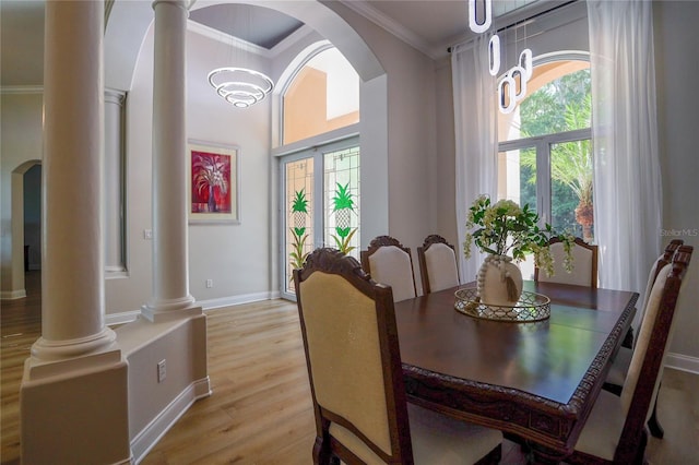 dining area featuring crown molding, light hardwood / wood-style flooring, a towering ceiling, and ornate columns