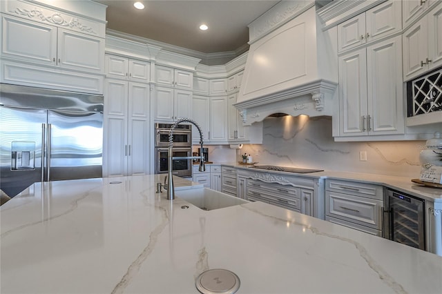 kitchen with sink, light stone counters, custom range hood, stainless steel appliances, and beverage cooler