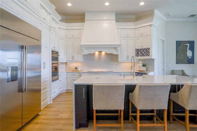 kitchen with sink, a breakfast bar, white cabinetry, stainless steel appliances, and custom exhaust hood