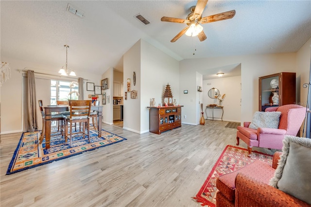 living room with a textured ceiling, light hardwood / wood-style flooring, lofted ceiling, and ceiling fan with notable chandelier