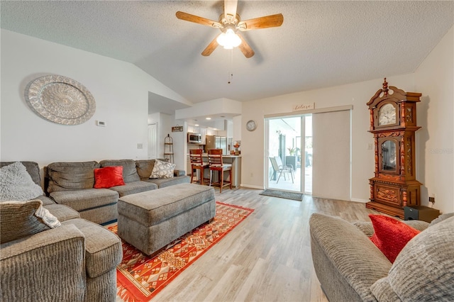 living room with ceiling fan, vaulted ceiling, a textured ceiling, and light wood-type flooring