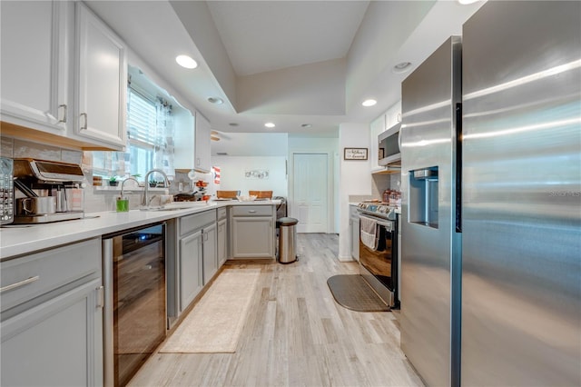 kitchen featuring appliances with stainless steel finishes, sink, beverage cooler, decorative backsplash, and light hardwood / wood-style flooring