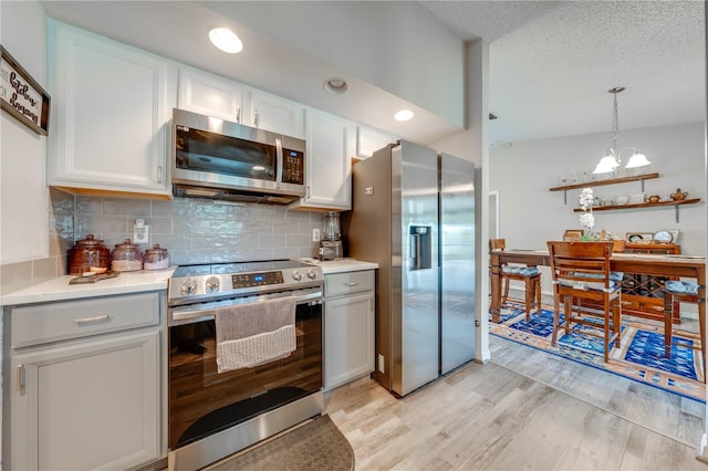 kitchen with appliances with stainless steel finishes, white cabinetry, backsplash, light hardwood / wood-style floors, and decorative light fixtures