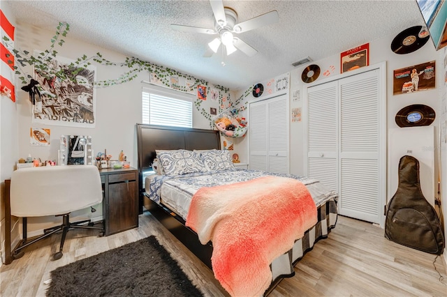 bedroom featuring multiple closets, a textured ceiling, ceiling fan, and light wood-type flooring