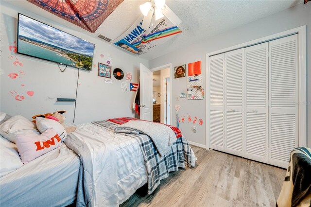 bedroom featuring a textured ceiling, light wood-type flooring, ceiling fan, and a closet